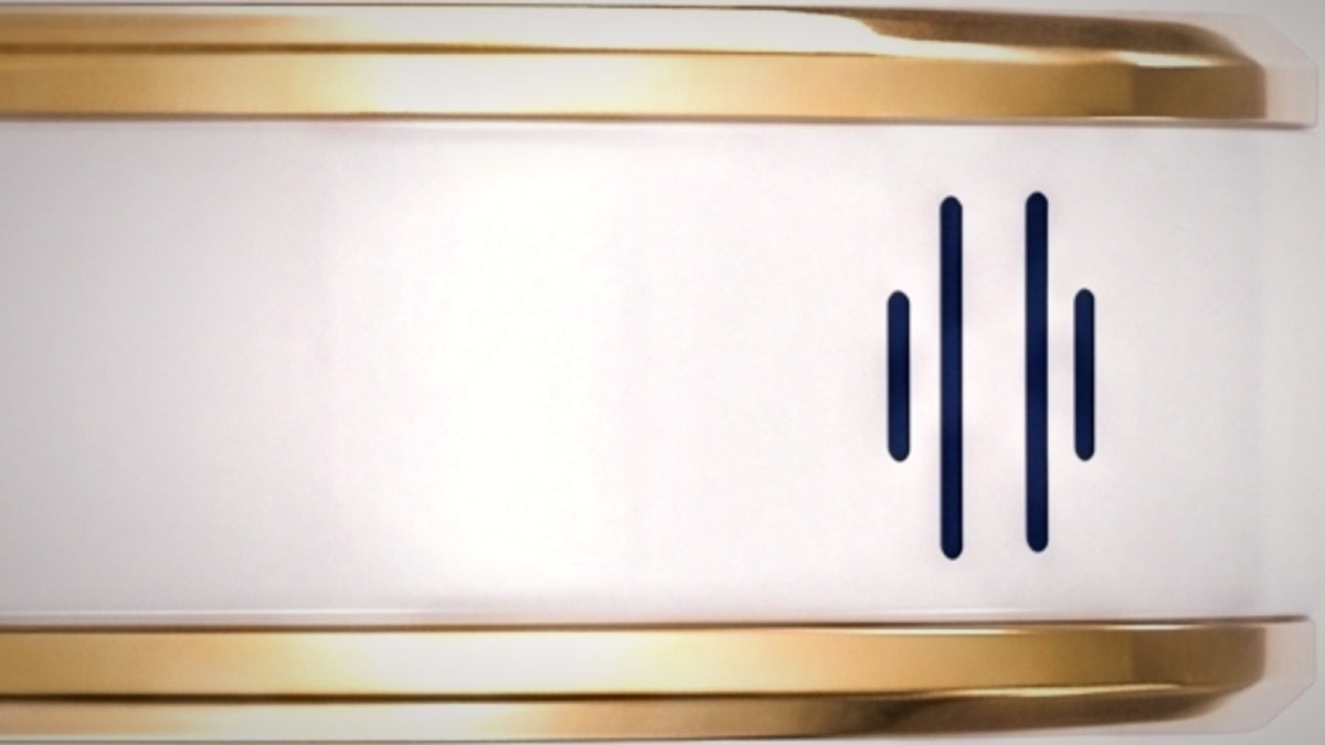 A close view of the Nodia Ring band curving through the frame, its champagne-gold rails and fine-ceramic channel carrying the recessed navy four-stroke engraving